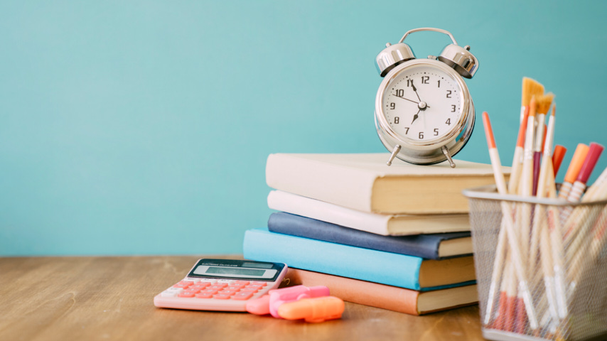 Despertador sobre libros y cubilete con pinceles.