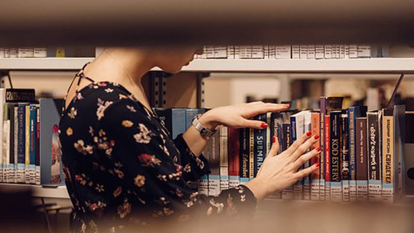 Mujer buscando libro en estante de bibli